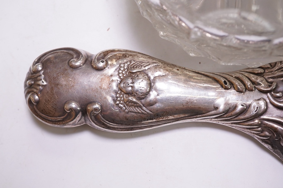 An Edwardian silver mounted hand mirror with Reynold's Angels decoration, William Neale Ltd, Chester, 1902, 26.3cm, together with a later silver mounted cut glass preserve jar and spoon. Condition - poor to fair